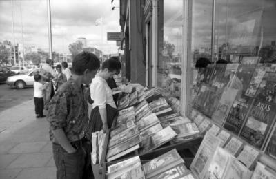 Black and white photograph of people browsing books on a street stall outside a shop window