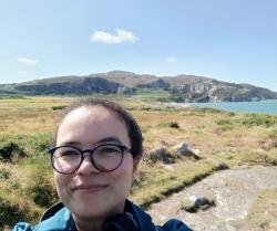 Ashley Williams outdoors with green hills and the sea behind her