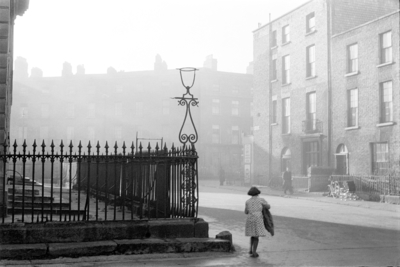 Black and white photograph of a misty Dublin street with Georgian houses and railings, and a child walking past