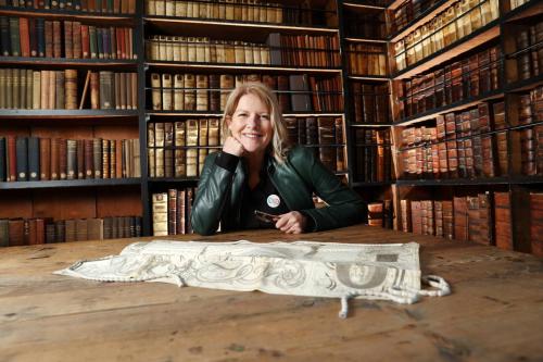 Flor MacCarthy seated at a table in a library, with an embroidered textile spread out in front of her