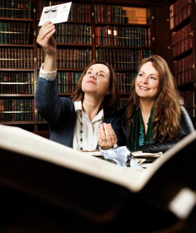 Niamh Ní Charra and Clodagh Finn holding a small item up to the light in a library