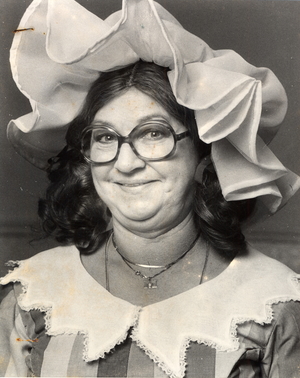 Black and white photograph of a pantomime dame as Sarah the Cook, in a large bonnet and glasses