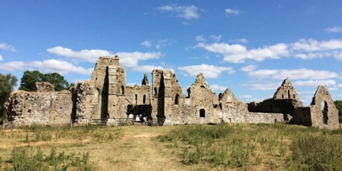 Ruins of a medieval abbey in a grassy field under a blue sky