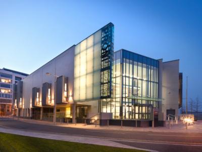 A modern glass-fronted archive building lit up at dusk